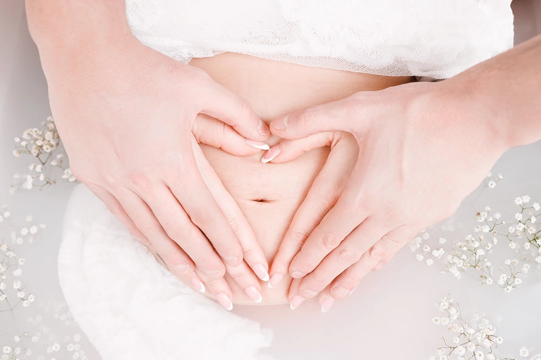 Photo grossesse bain de lait avec les mains en coeur sur le ventre