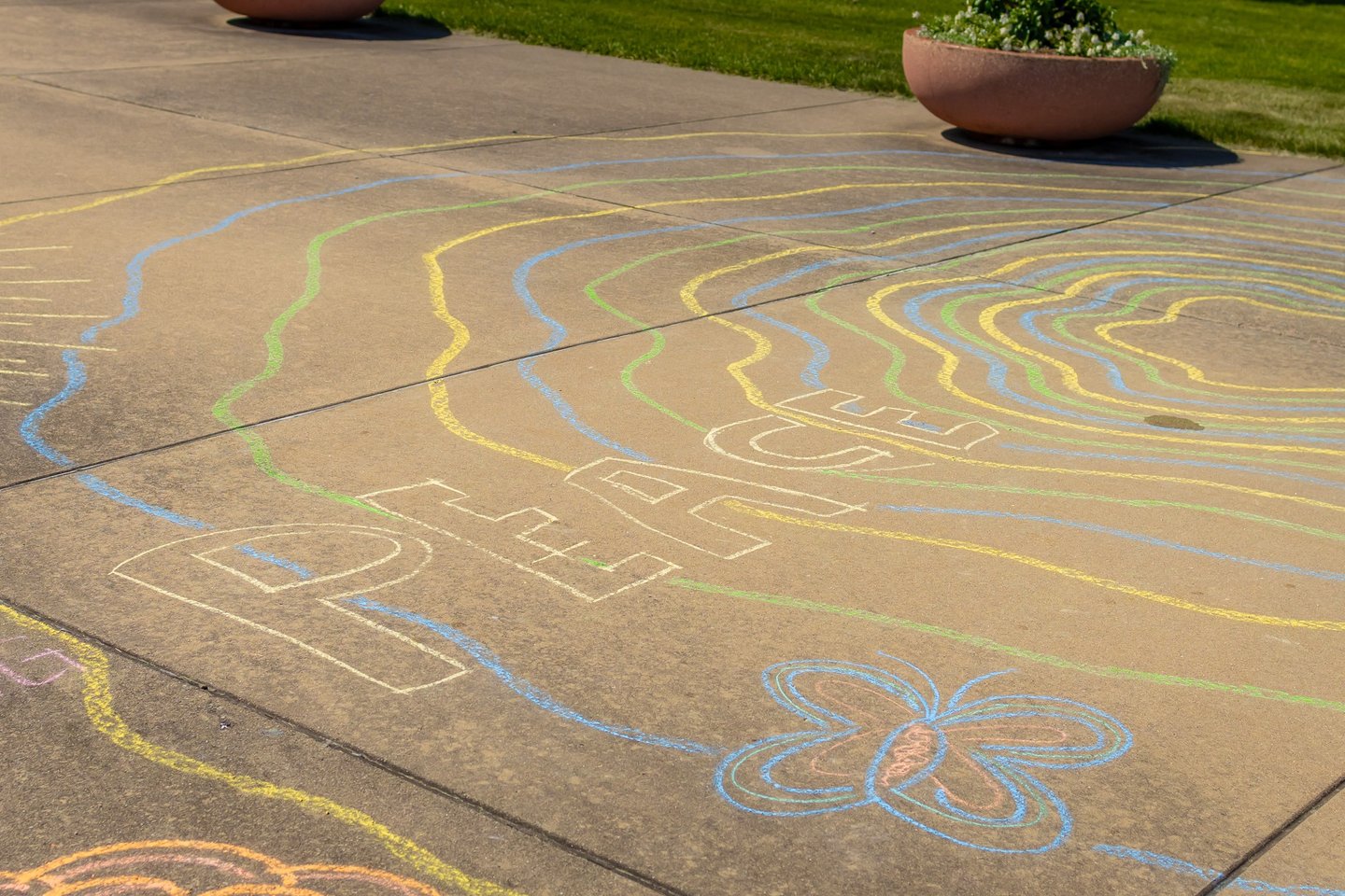 Colorful chalk art on a concrete sidewalk featuring the word PEACE and a butterfly drawing.