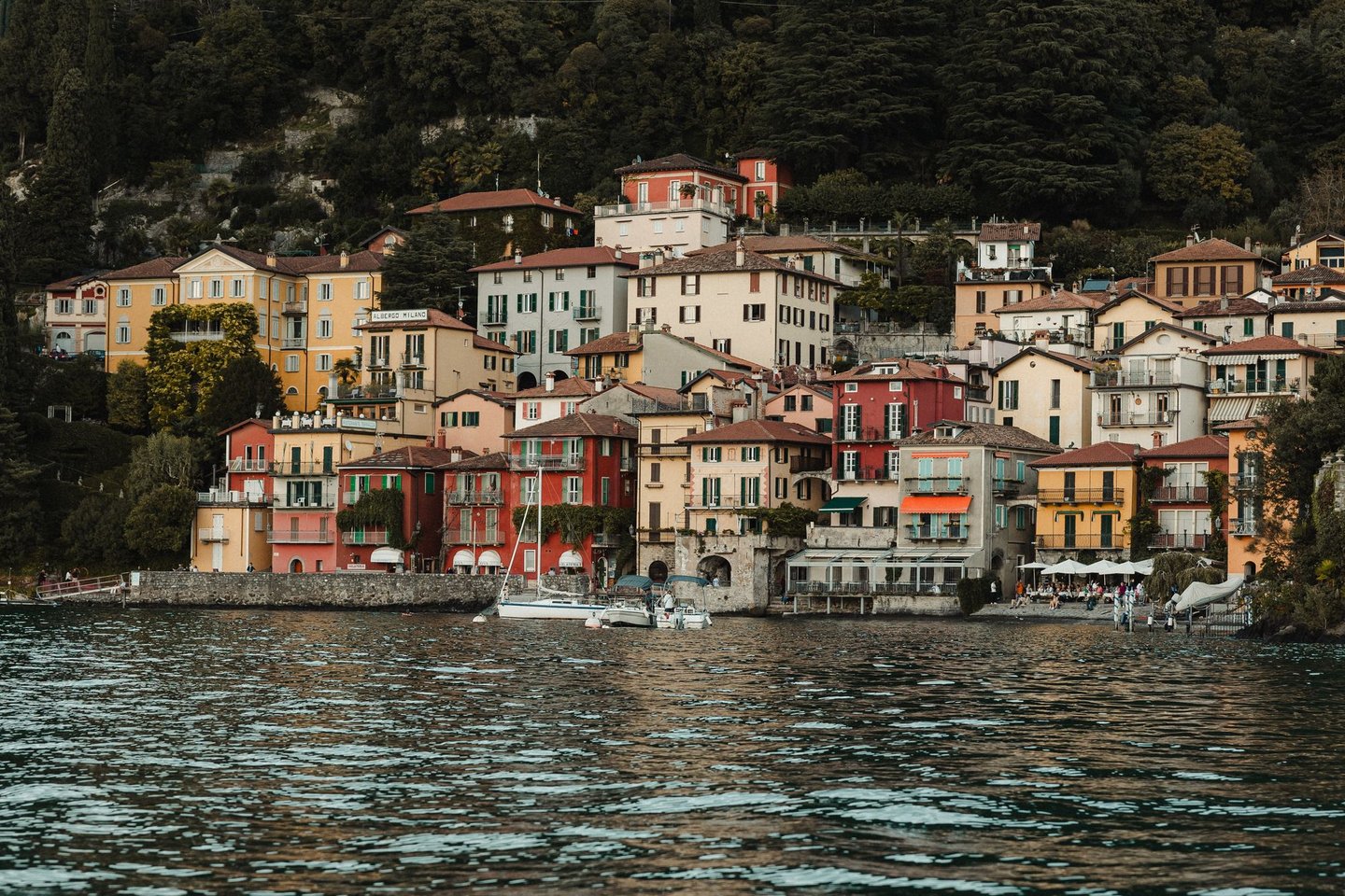 a bunch of houses on a hill with a boat in the water varenna lake como