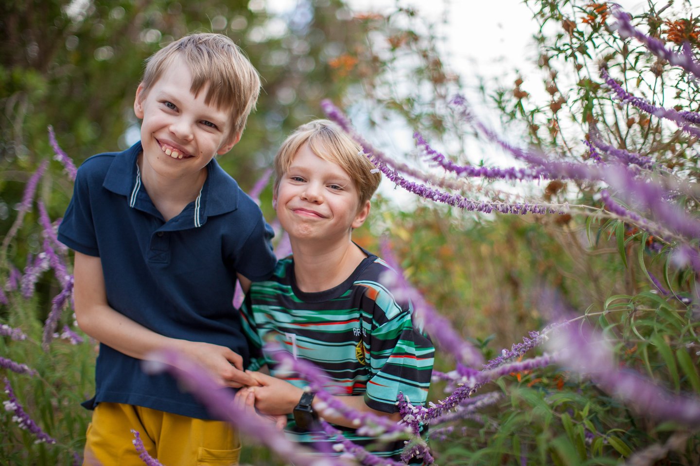 Two brothers share a happy moment surrounded by purple wildflowers in Pestana Grand, Madeira, natural lifestyle family photo.