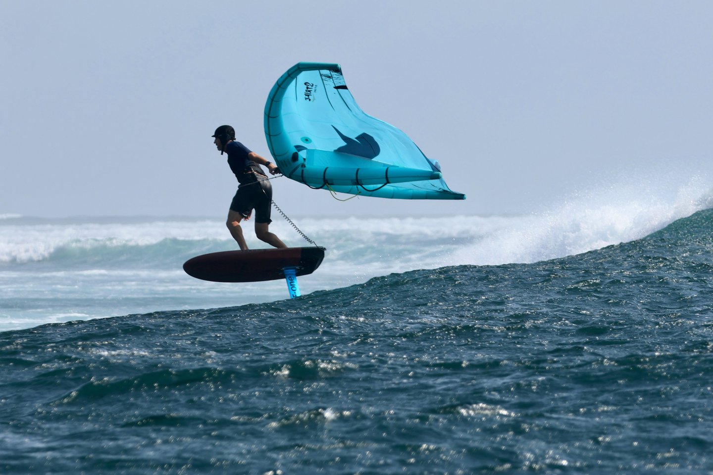 a man is holding a wing on a  foil board in the water, over a wave