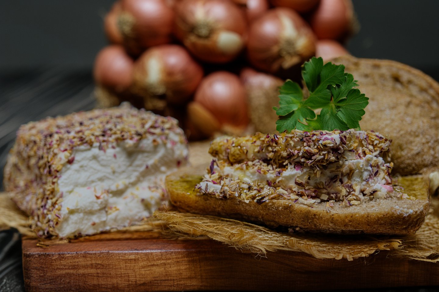 Herbed goat cheese spread on crusty bread with fresh shallots on a rustic wooden board.