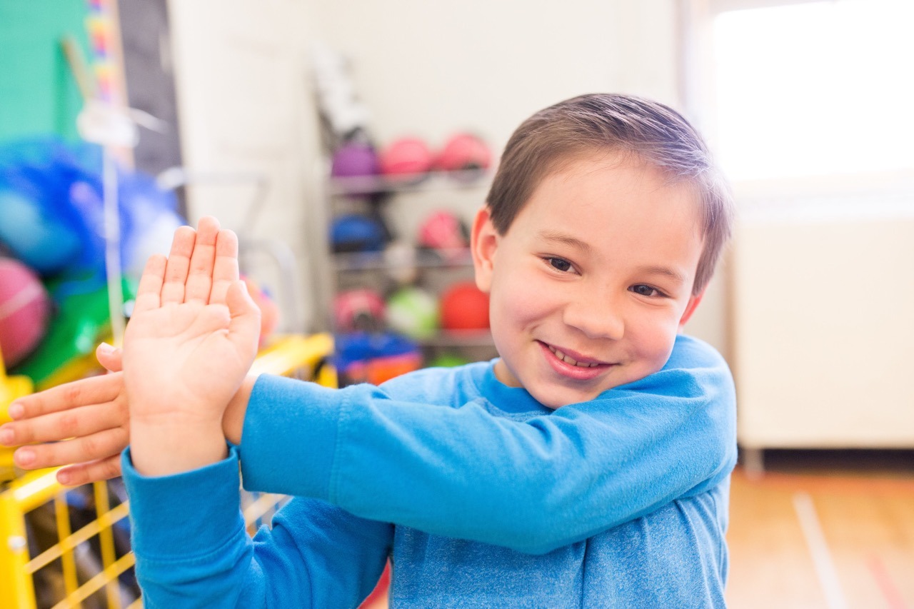 Elementary boy does a shoulder stretch.