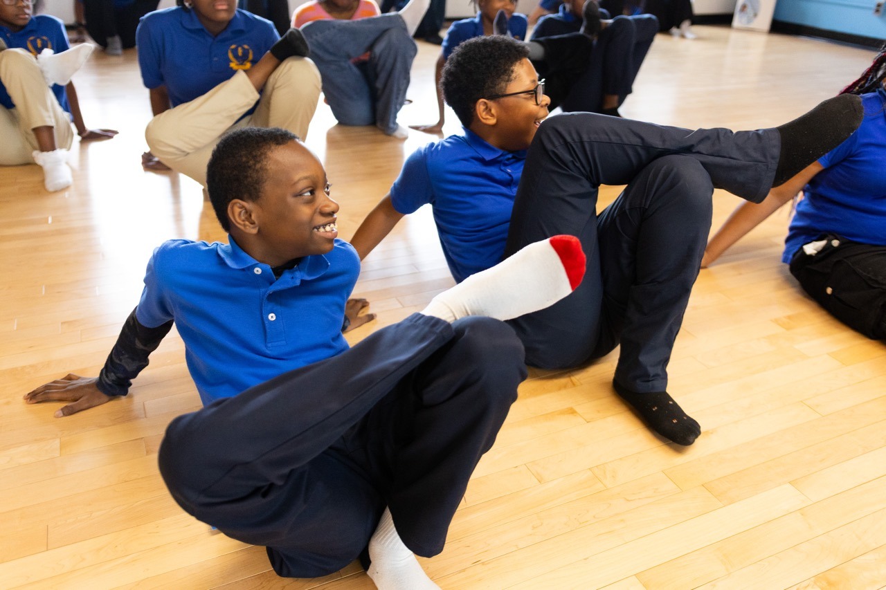 Students do a leg stretch together.