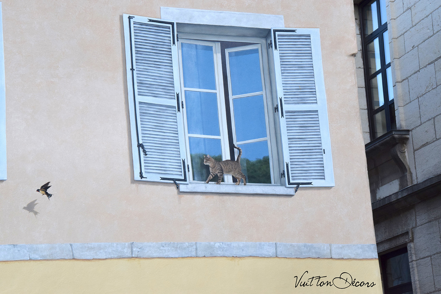 Fenêtre en trompe-l'oeil à Moirans-en-Montagne: un chat au bord d'une fenêtre regarde un oiseau.