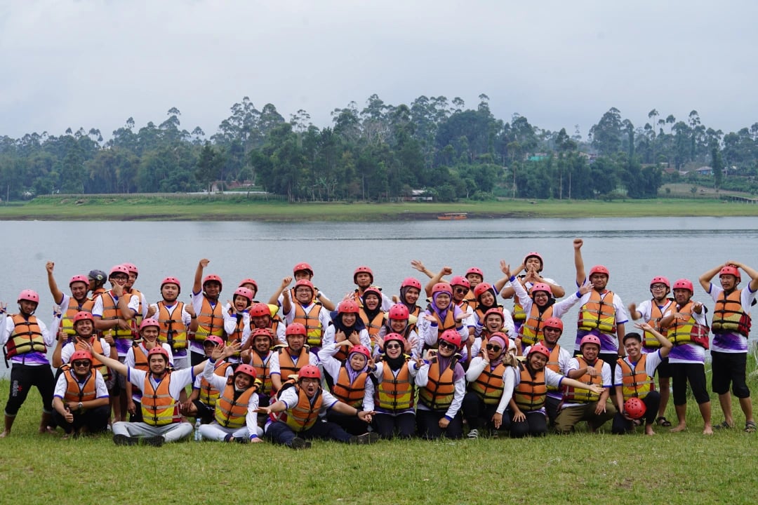 Sekelompok peserta rafting pangalengan berfoto bersama di tepi danau, mengenakan helm merah dan pelampung oranye,
