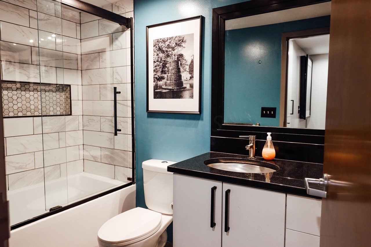 Modern bathroom with blue walls, a white marble tile shower, and a black granite vanity.