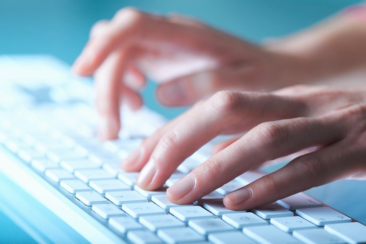 Close-up of hands typing on a modern white computer keyboard for office productivity.