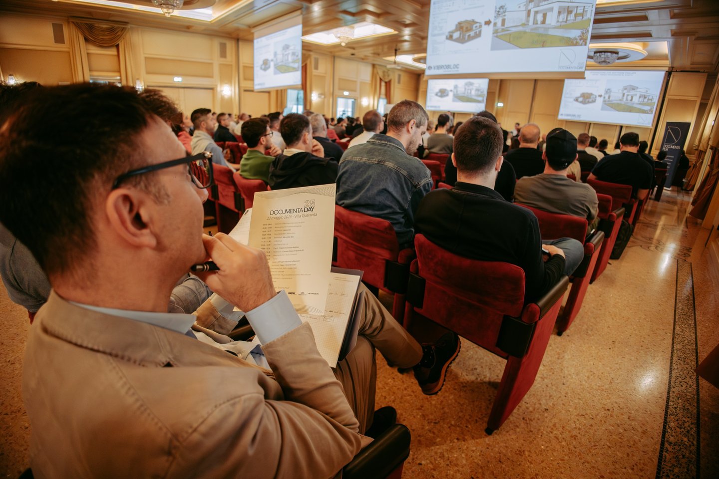 Professional audience attending a business seminar with architectural presentations on overhead screens.