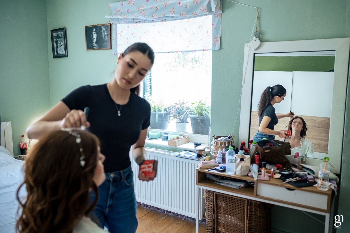Bride sitting at vanity while makeup artist adds finishing touches — elegant bridal photo prep
