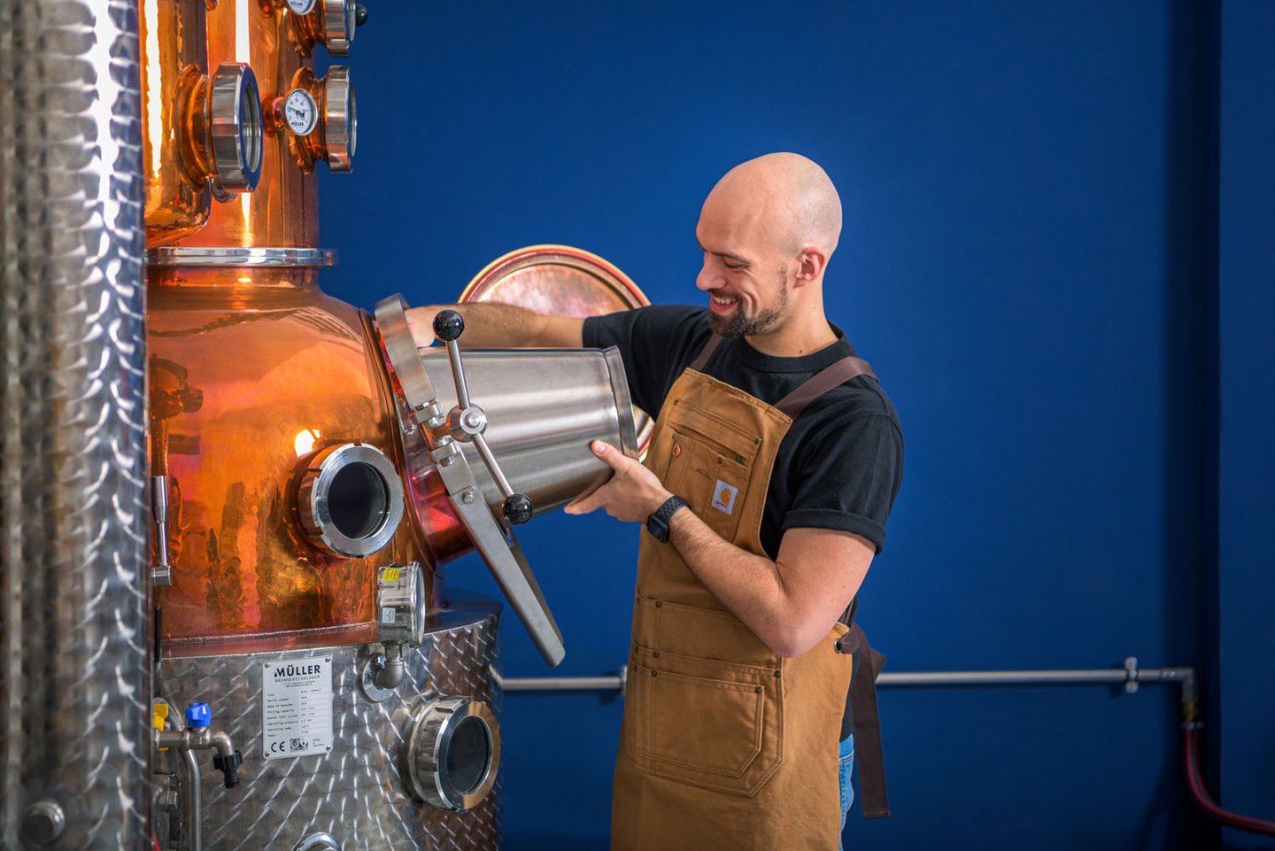 Mastro distillatore che sta caricando il suo alambicco con un secchio di acciaio in mano