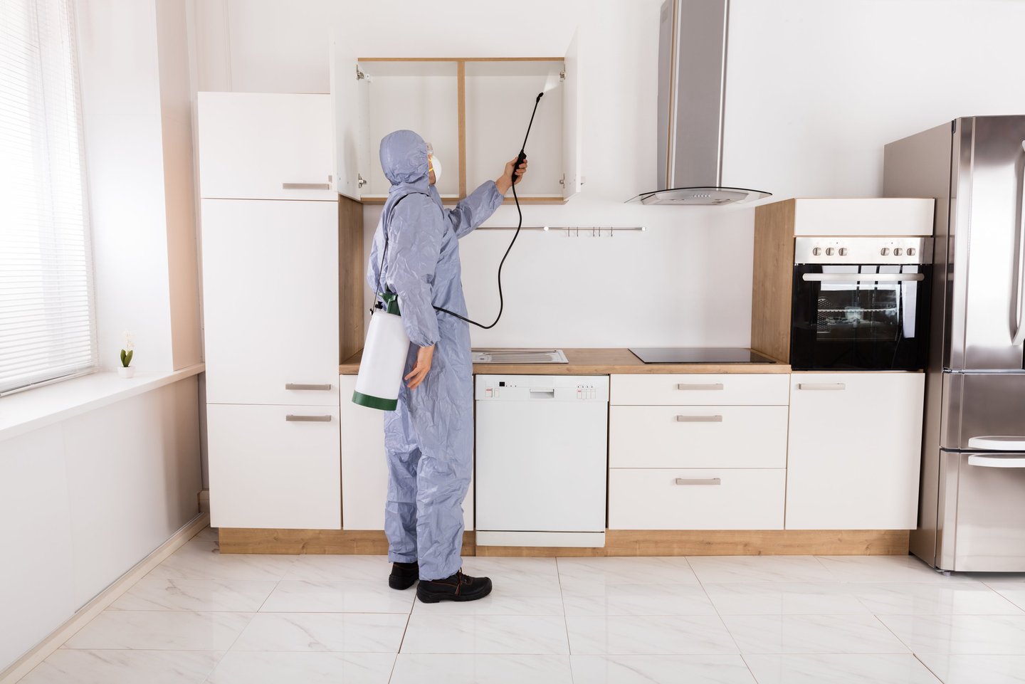 Professional pest control worker in a hazmat suit spraying kitchen cabinets for pest extermination.