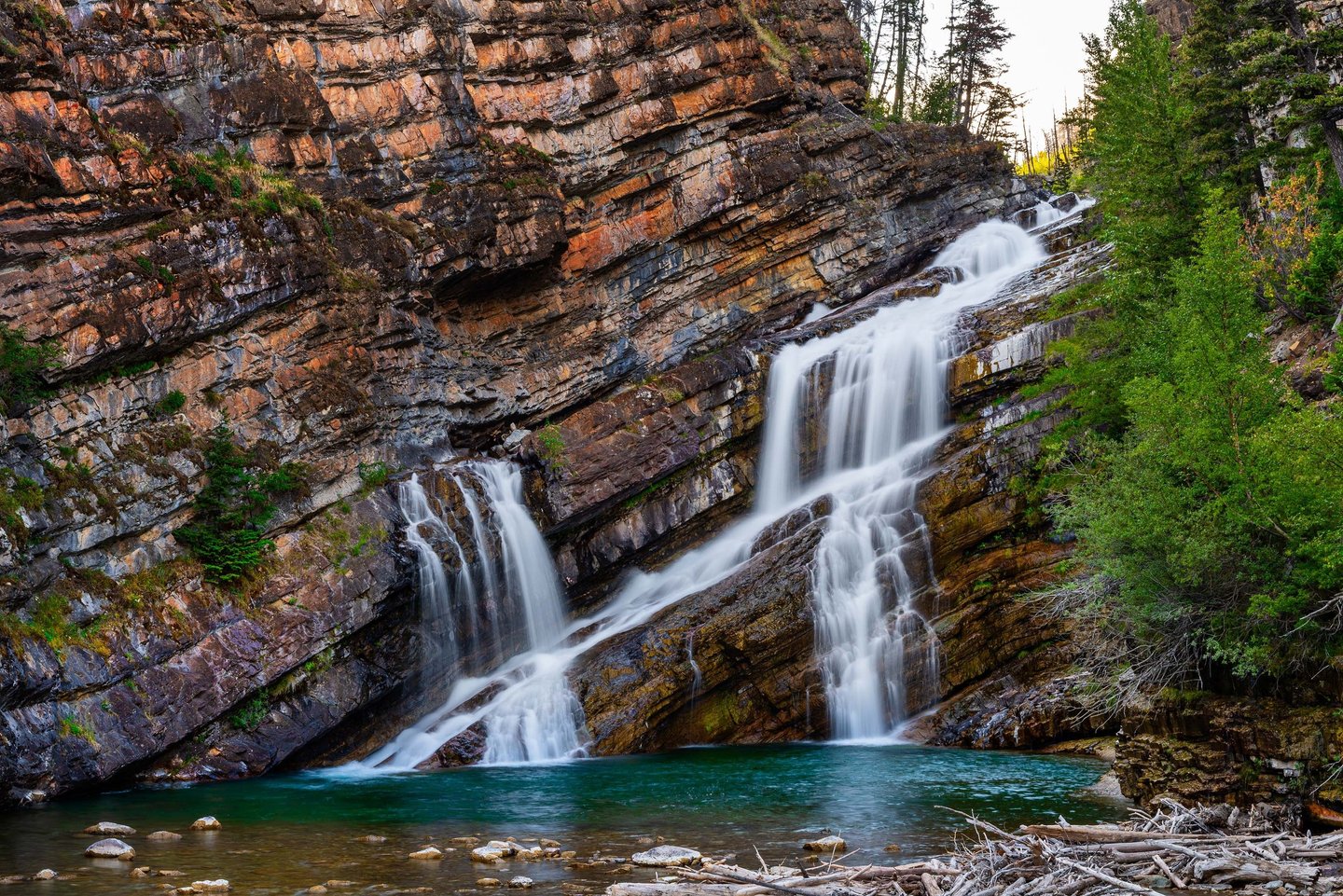 Cameron Falls cascading over layered red rock into a turquoise pool in Waterton Lakes National Park,