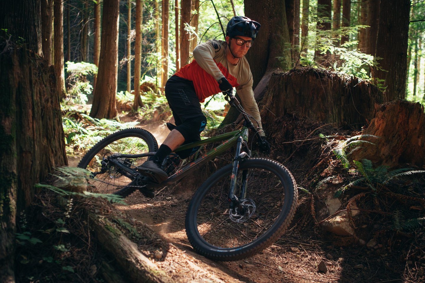 A mountain biker wearing a helmet navigates a steep dirt berm on a forest trail.