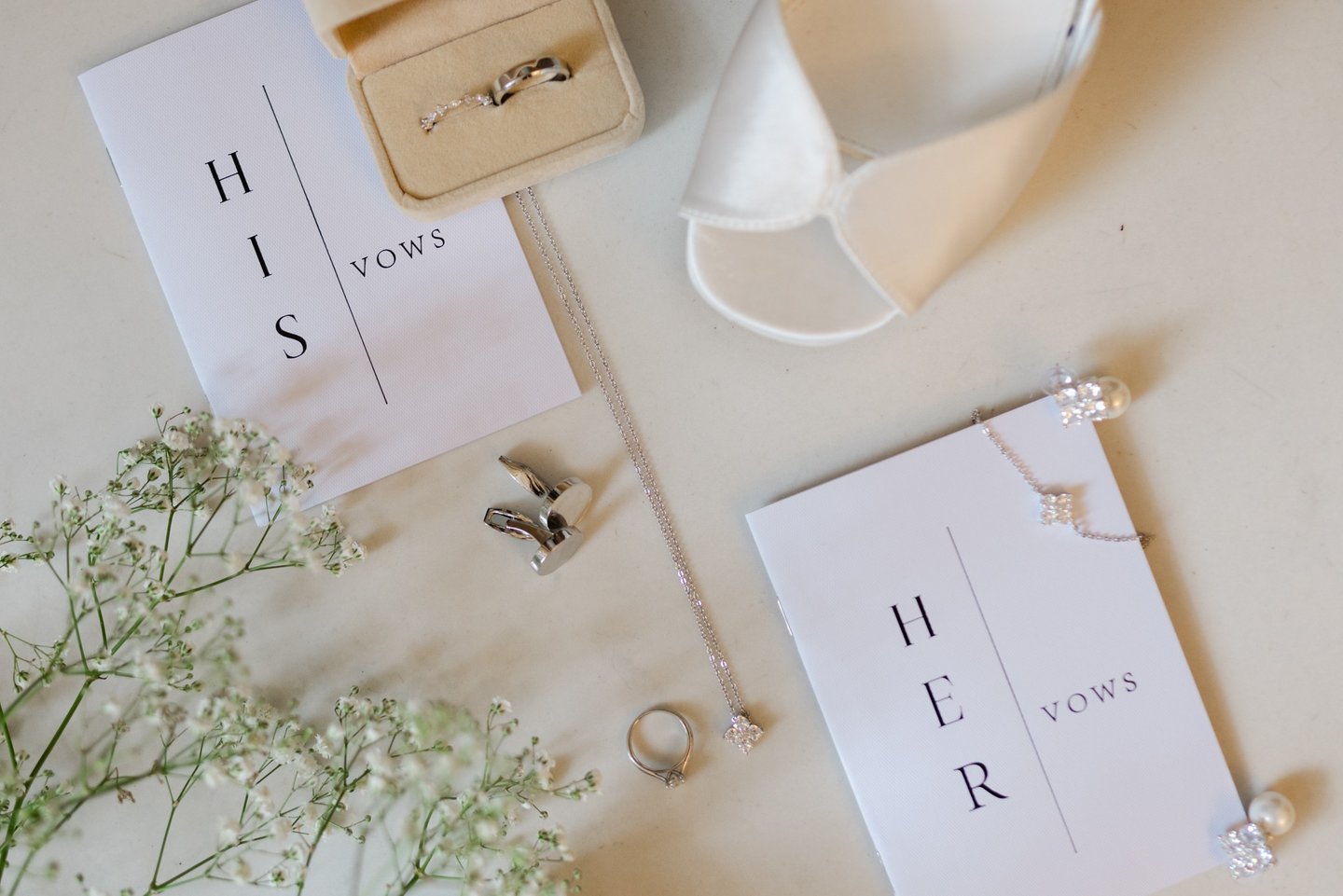 Wedding detail flat lay featuring rings, vow book, necklace, cufflinks and bridal shoes