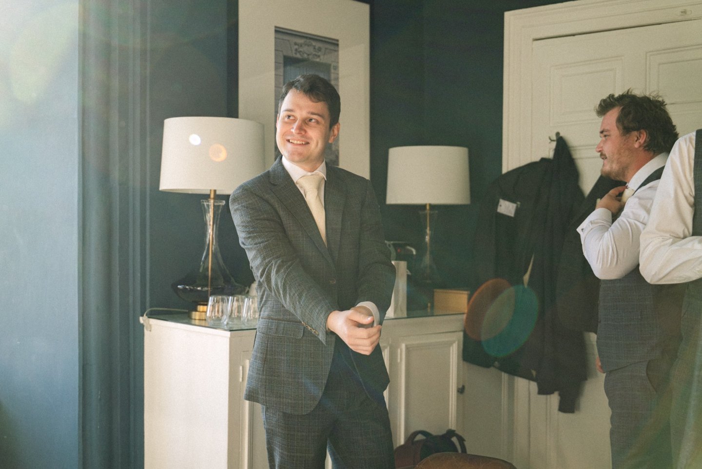 Groom smiling while making final adjustments to his shirt sleeves during wedding morning preparation