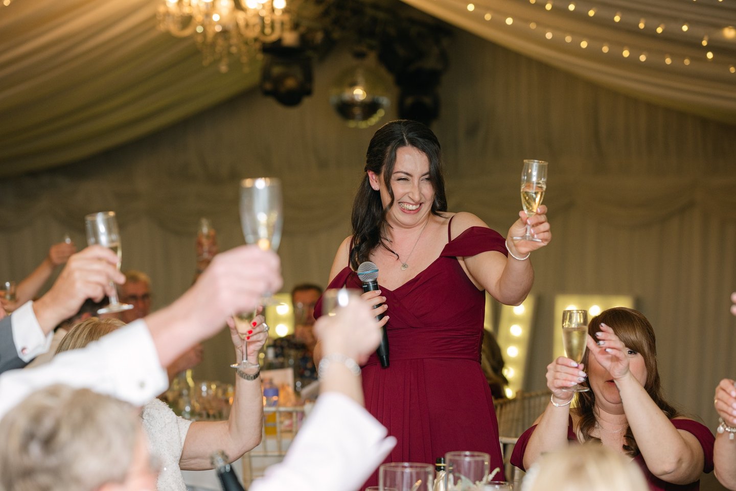Bridesmaid in a red dress raising a glass to the couple at The Mill House Hotel