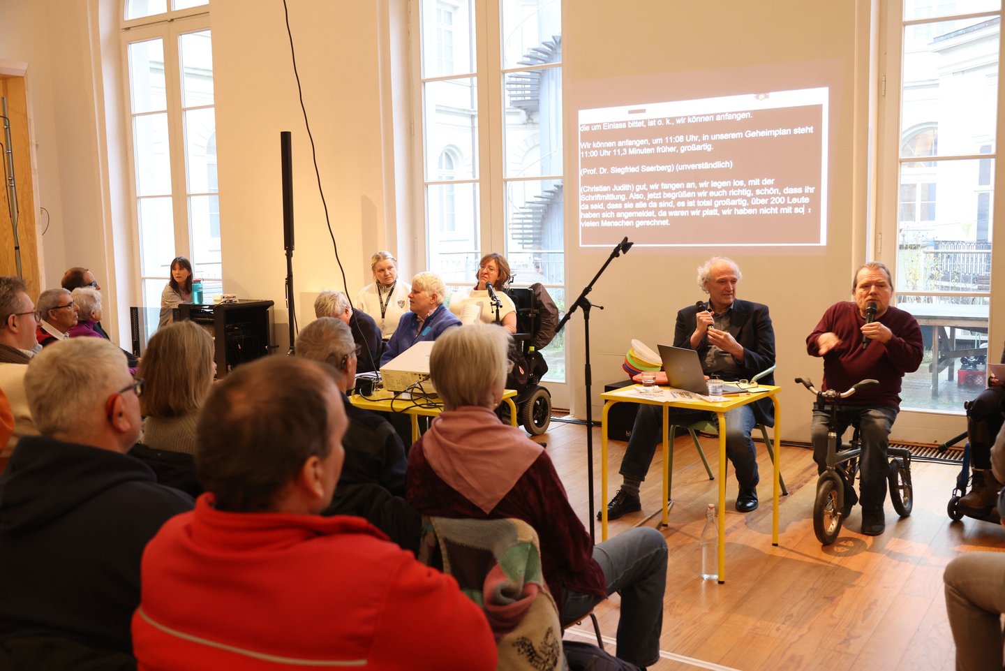 Zwei Menschen mit Behinderung sprechen vor einer Gruppe von Menschen