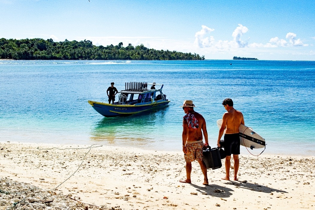 two men walking on the beach with a boat in the background