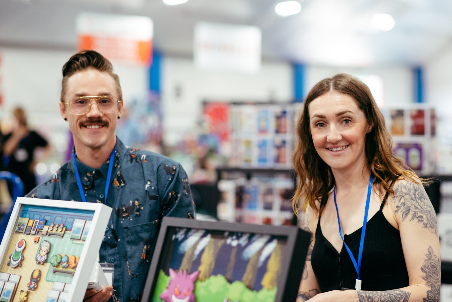 Two smiling vendors stand in front of the video game themed art they have for sale.