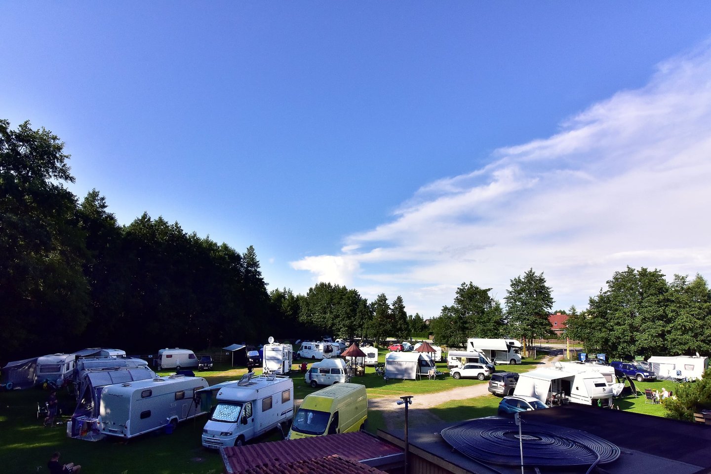 Aerial view of campsite Karkle Camp with vans and motorhomes parked near trees under a blue sky.