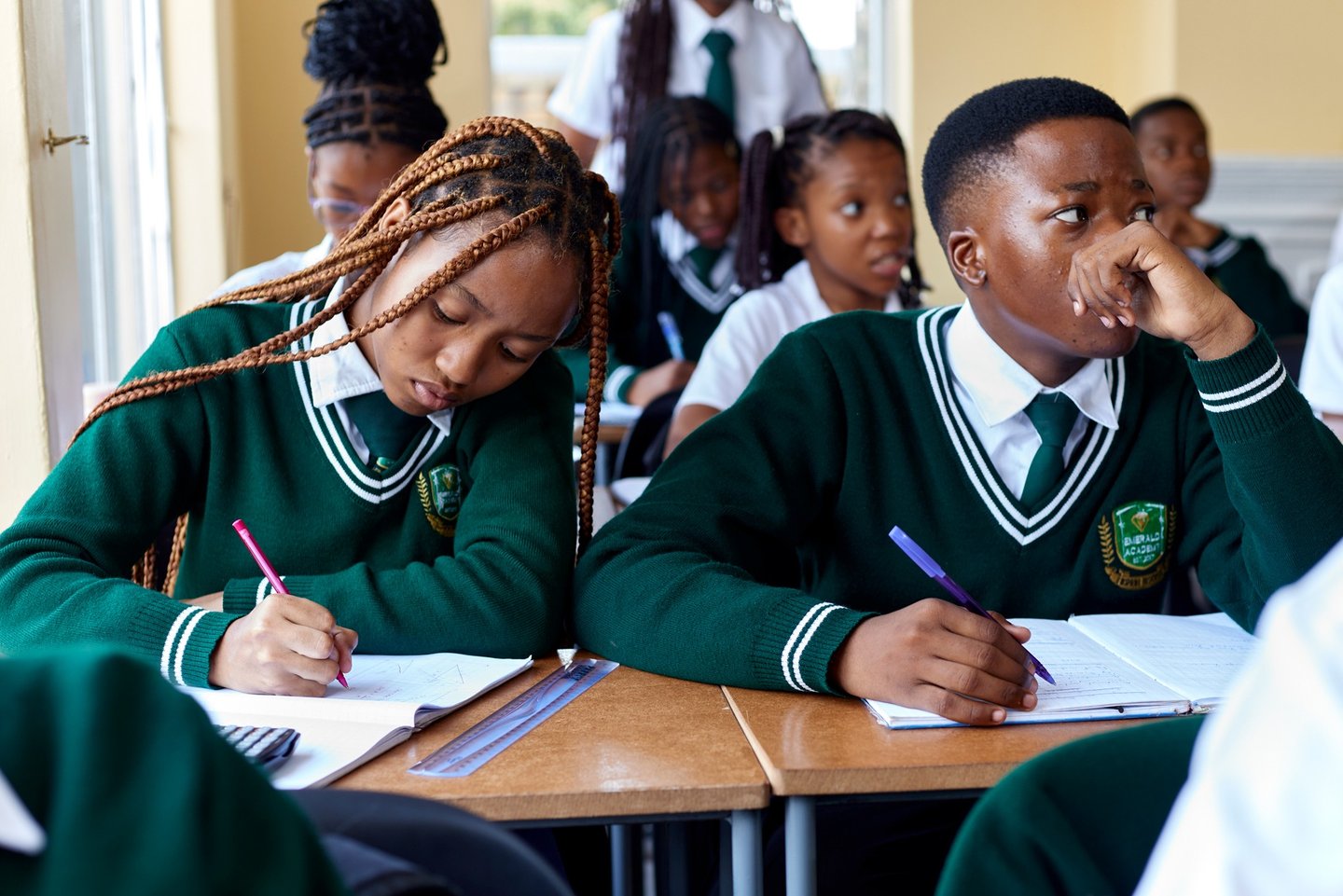 Students in green school uniforms taking notes and studying in a high school classroom.