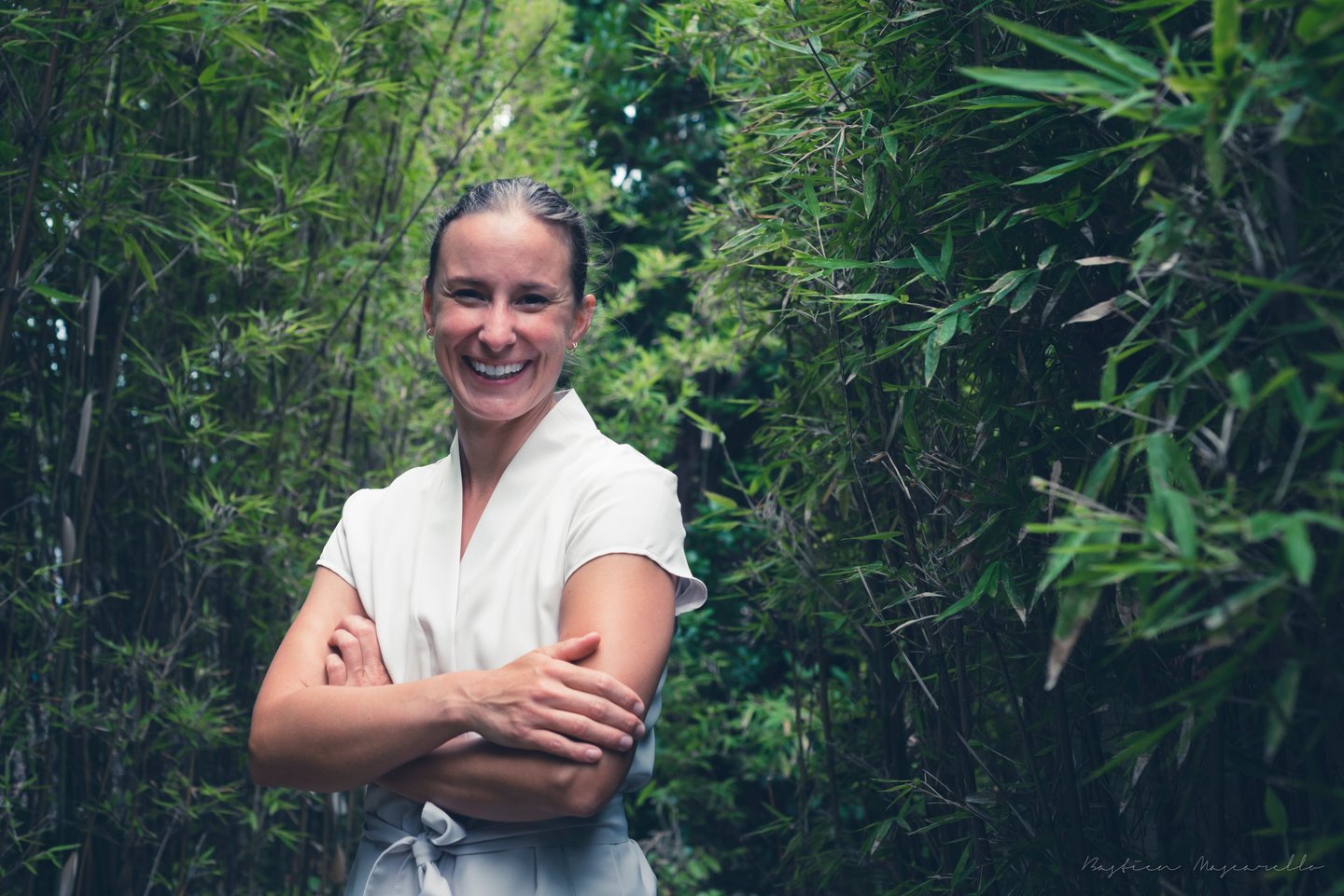 Portrait d'Anaïs plein sourire en blouse de soin beige dans une allée de bambous
