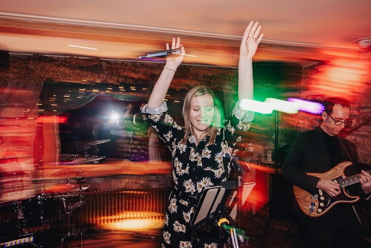 a woman in a floral jumpsuit dancing with a guitar at wedding party