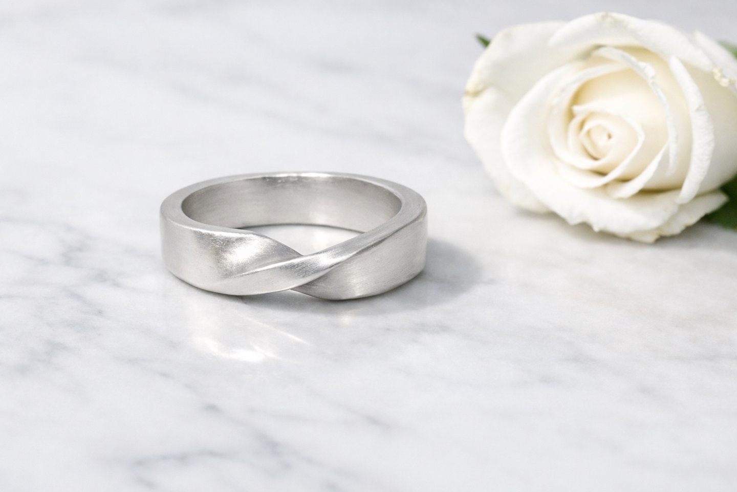 A satin 999 fine silver twisted mobius ring rests on a white marble surface with soft gray veining, 