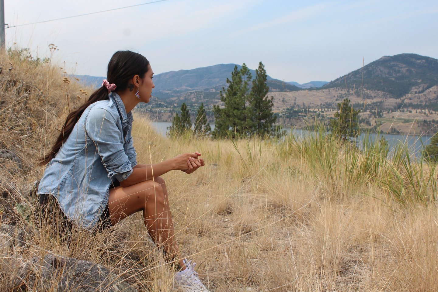 a person sitting on a hill looking at a lake in the distance