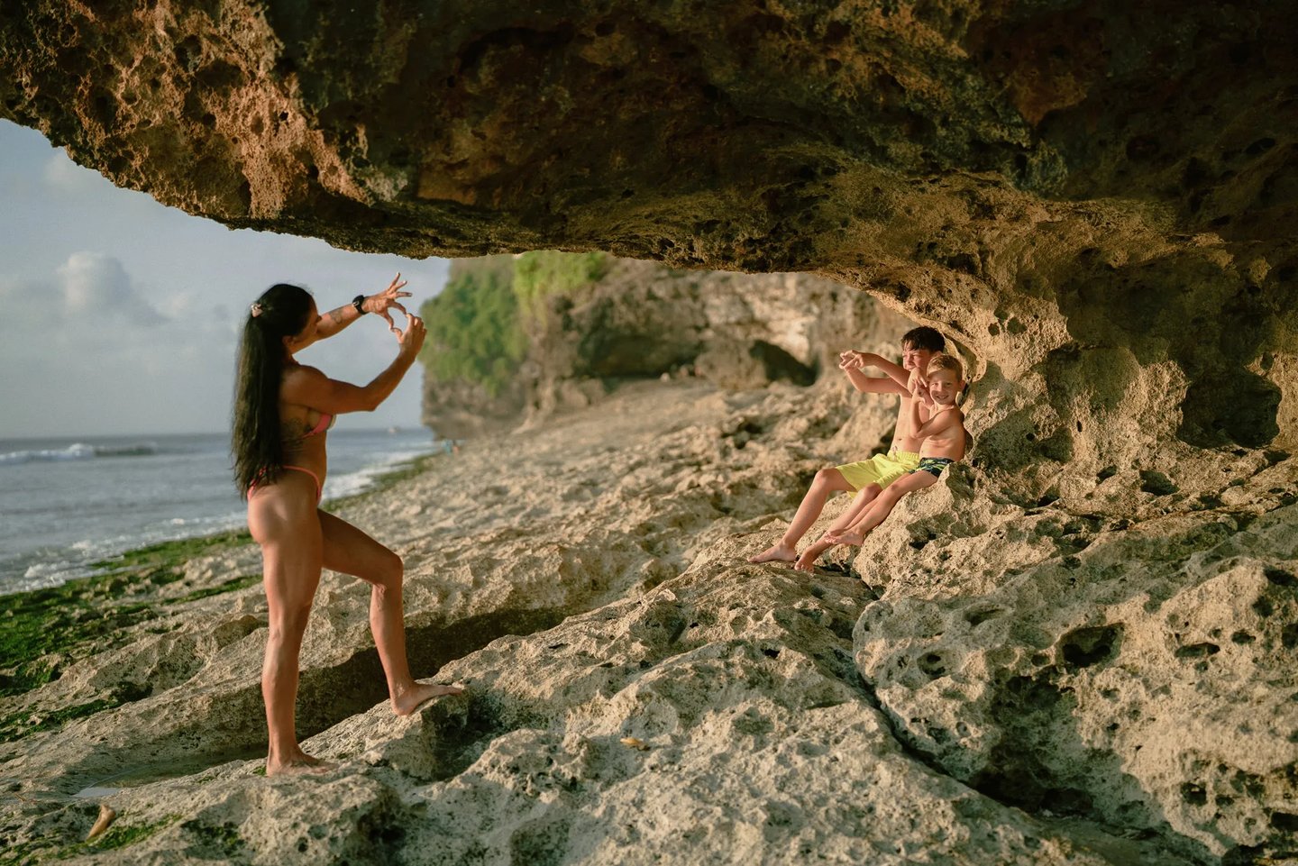 Mother capturing memories of her children near a natural rock cave at Dreamland Beach Bali.