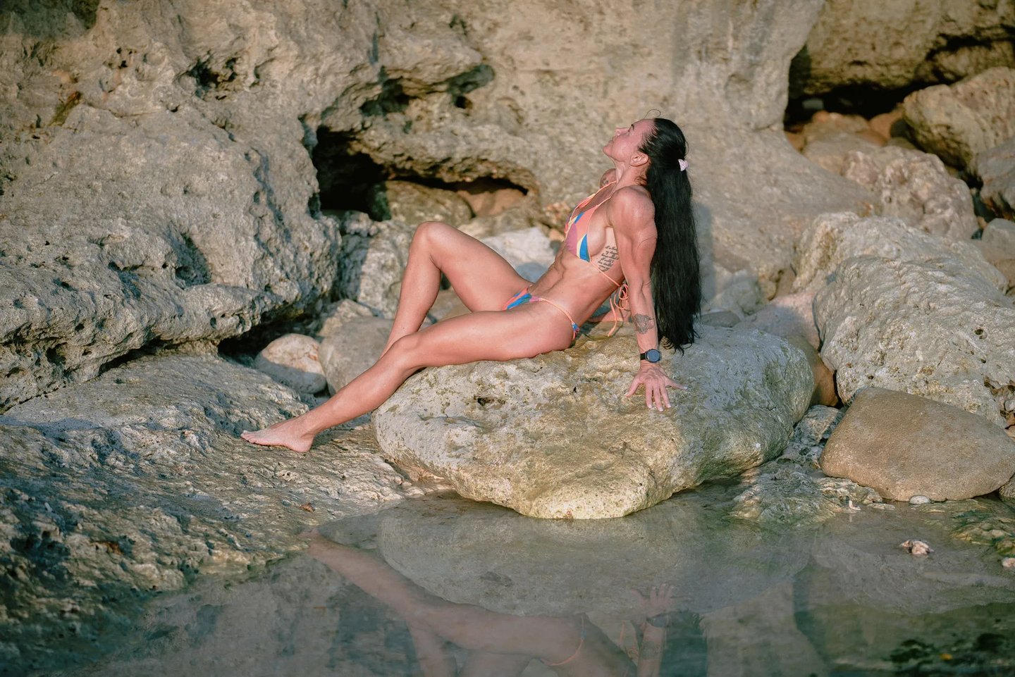 Mother relaxing on the rocky shoreline during a sunset family photography session at Dreamland Beach Bali.