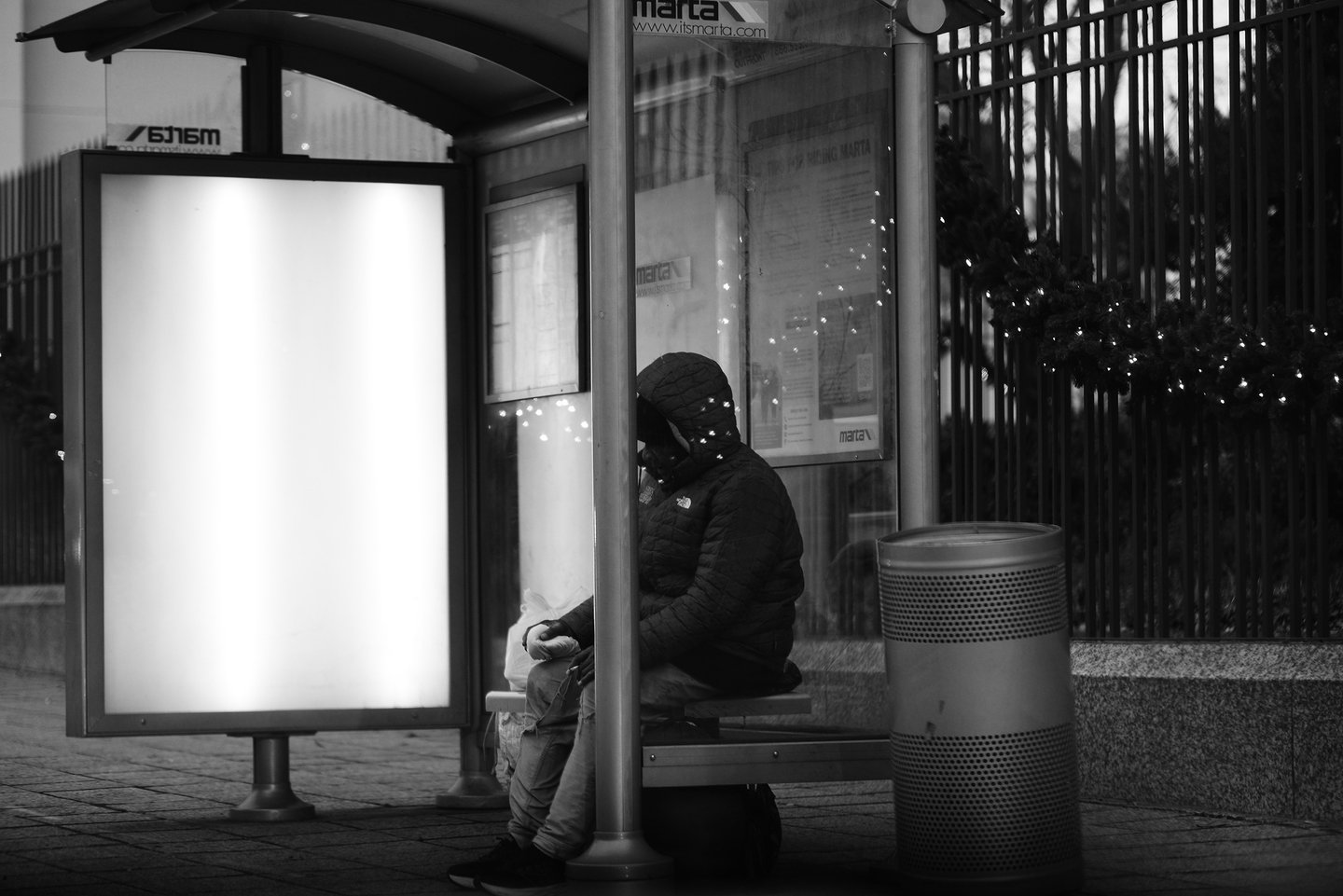 A person in a hooded puffer jacket sits at a black and white MARTA bus stop at night.