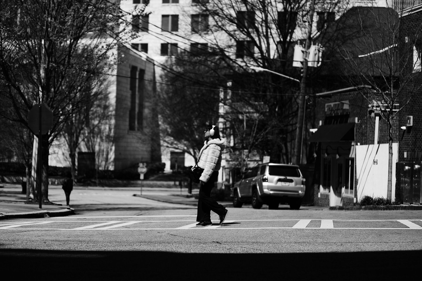 Black and white street photography of a person with headphones walking across a city crosswalk.
