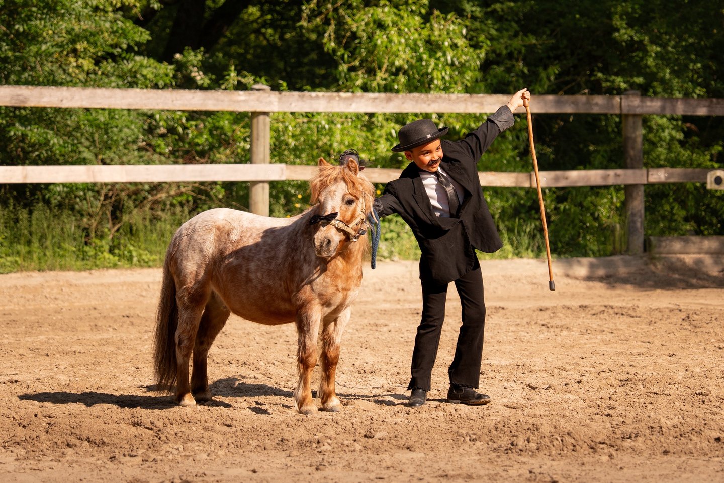 a girl in a suit and hat standing next to a horse