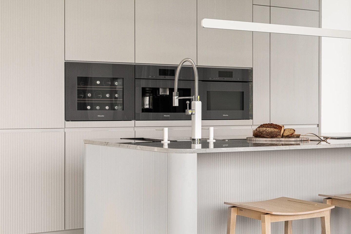 Nowoczesna kuchnia, beżowe ryflowane fronty, sprzęt do zabudowy Miele i kamienna wyspa.