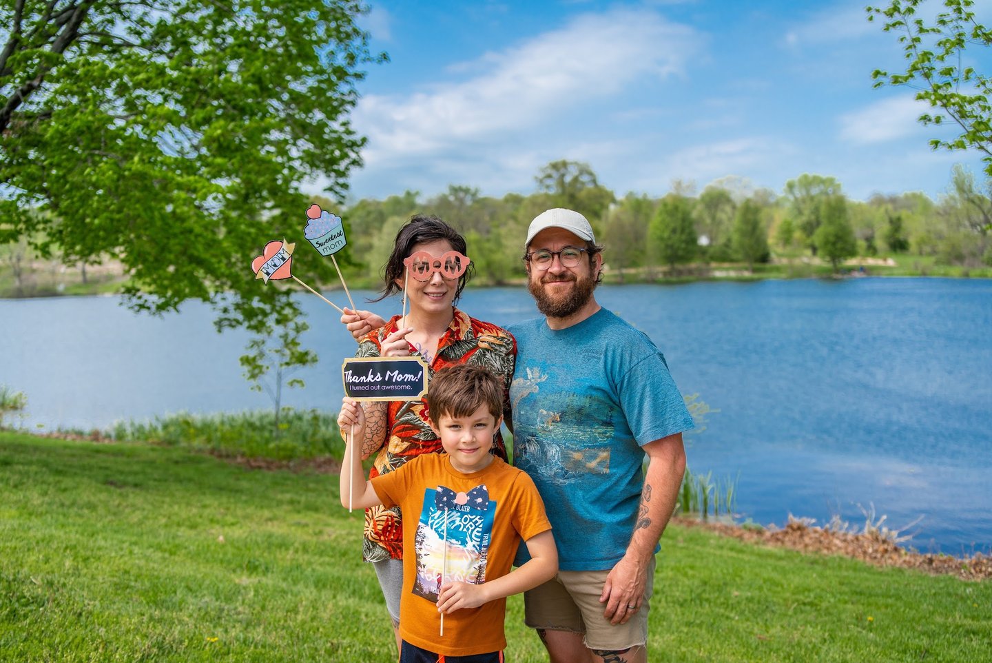Staged photo of a couple with a young child in front of a lake, holding up paper props
