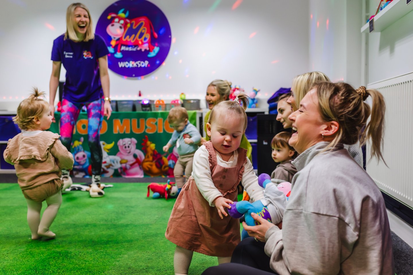 A young Mini Moo attendee and her Mum smiling and laughing, playing with a soft toy.