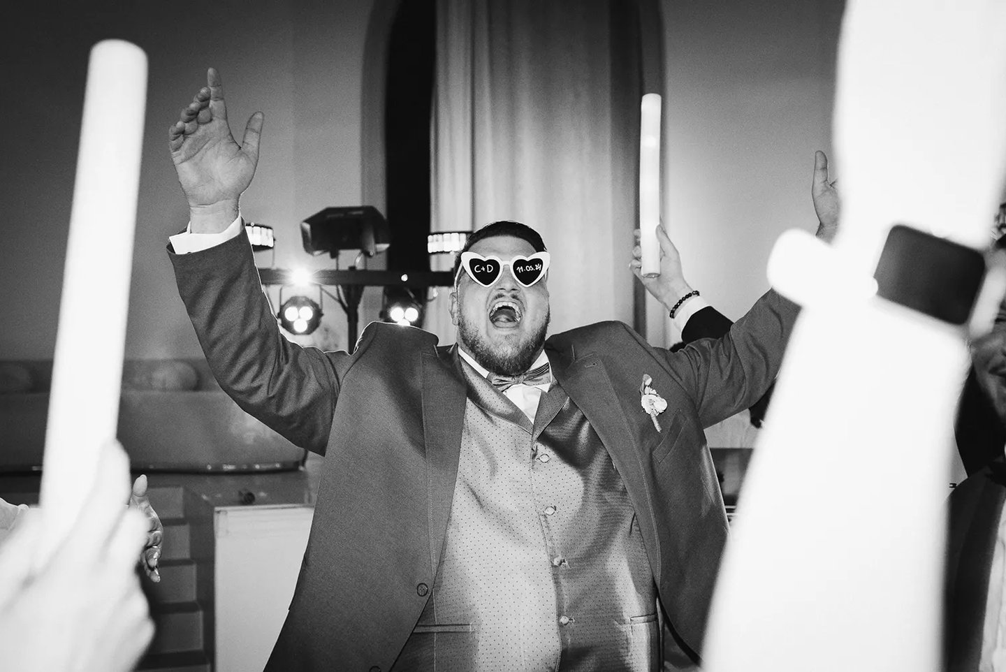 Le marié, lunettes de fête sur le nez, bras levés et sourire éclatant, profite de la soirée.