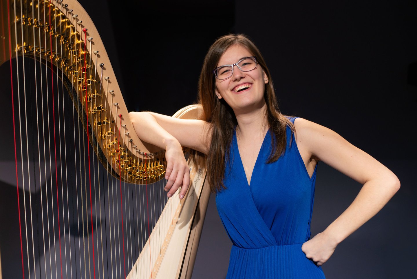 Clara Busemann steht lachen an einer Konzertharfe und hat einen Arm locker über ihre harfe gelegt