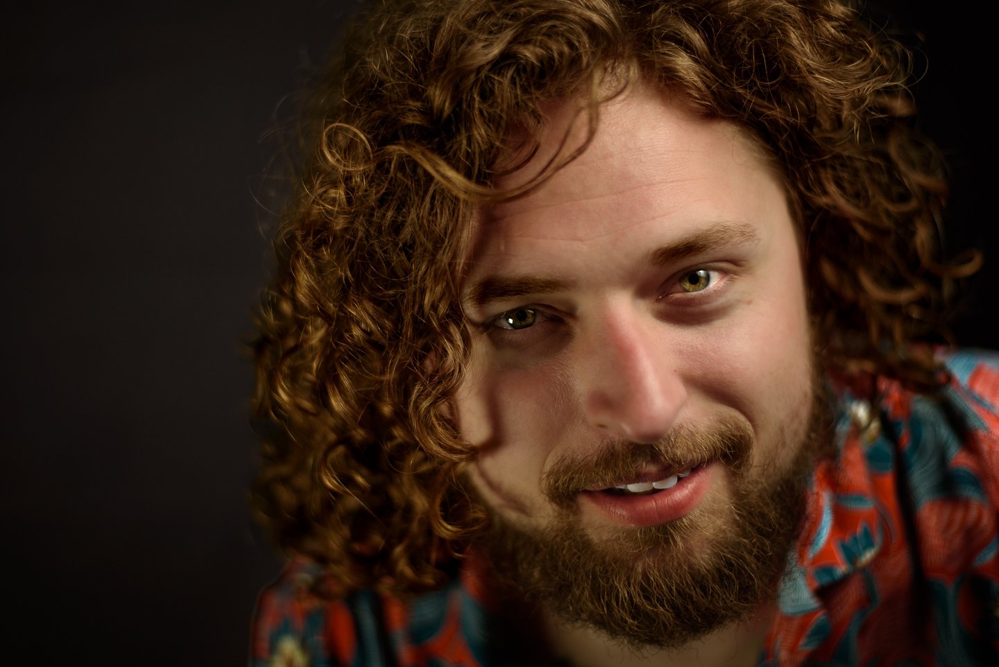 Close-up portrait of a smiling man with long curly brown hair and a beard.