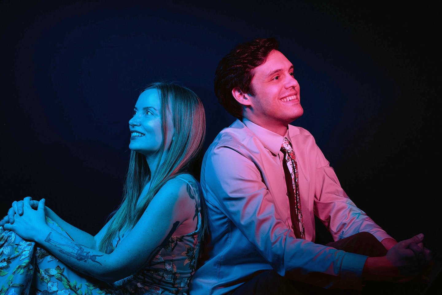 a man in red light and woman in blue light sitting back to back looking at opposite direction