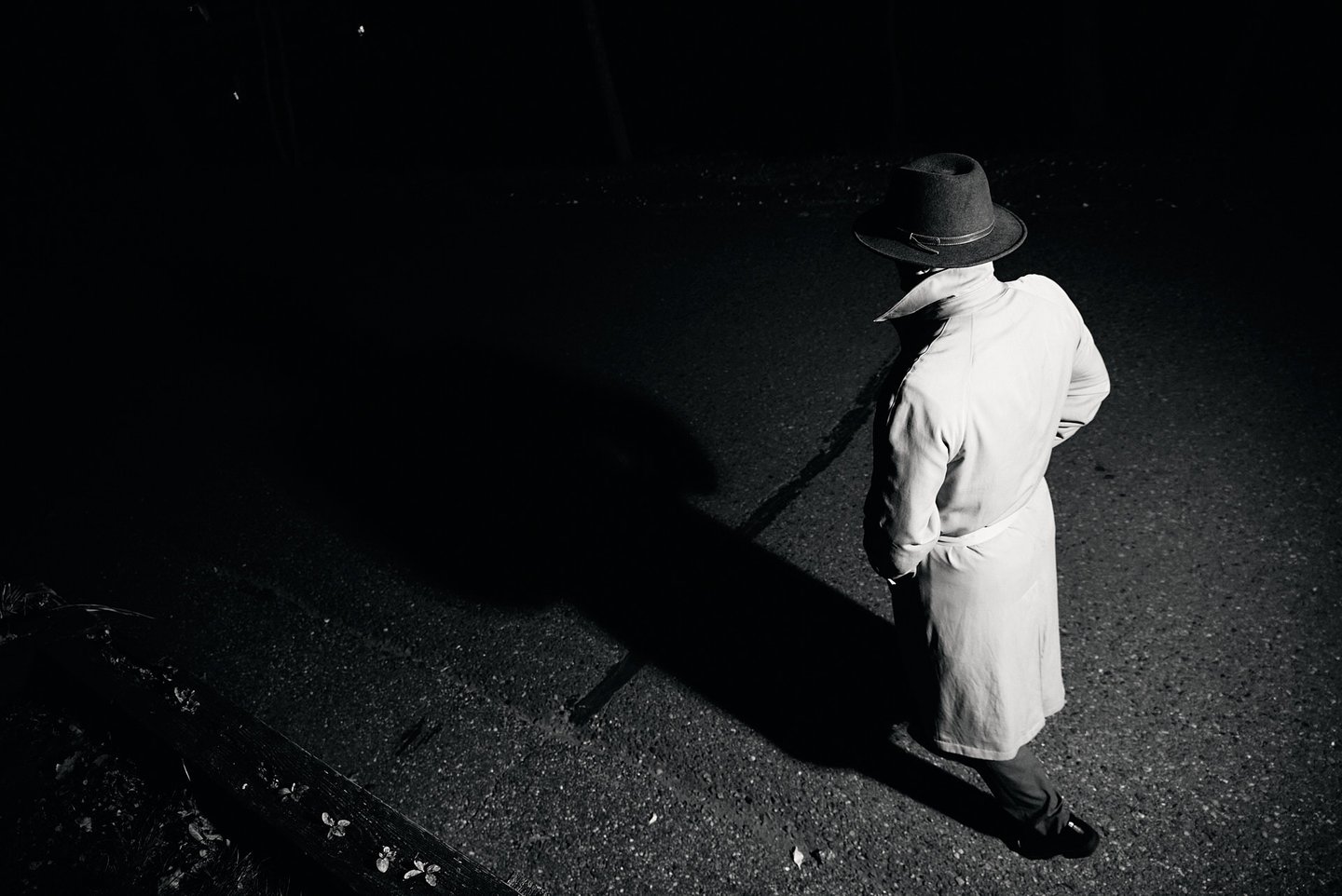 a man in a long coat and hat walking at night time