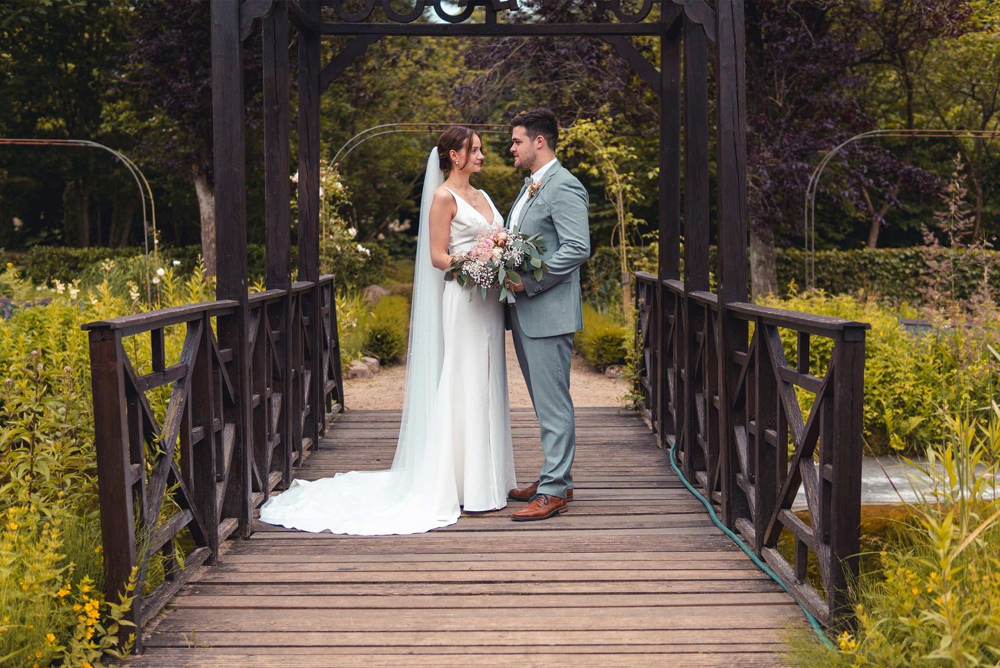 Brautpaar steht verliebt auf einer Holzbrücke im Grünen. Romantische Hochzeitsfotografie von Just Perspectives.