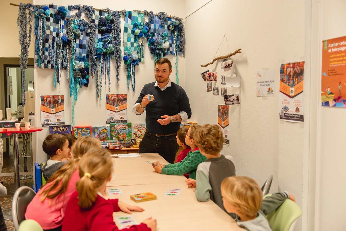 Animateur expliquant un jeu à un groupe d’enfants dans un espace coloré et ludique.