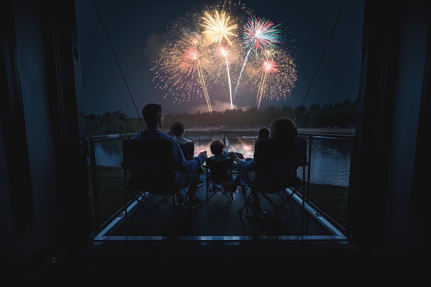 a family watching fireworks in the night sky on an RV deck