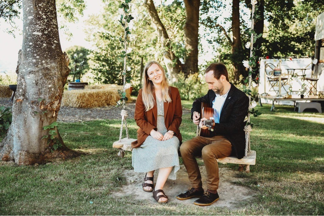 a man and woman sitting on a swing with a guitar at wedding