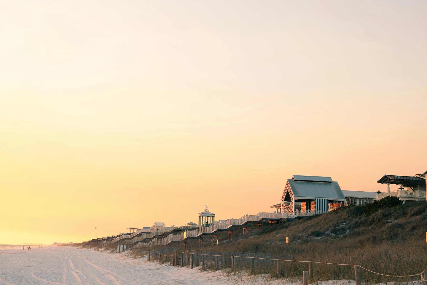 Luxury beachfront pavilions and coastal architecture along a white sand beach at sunset.