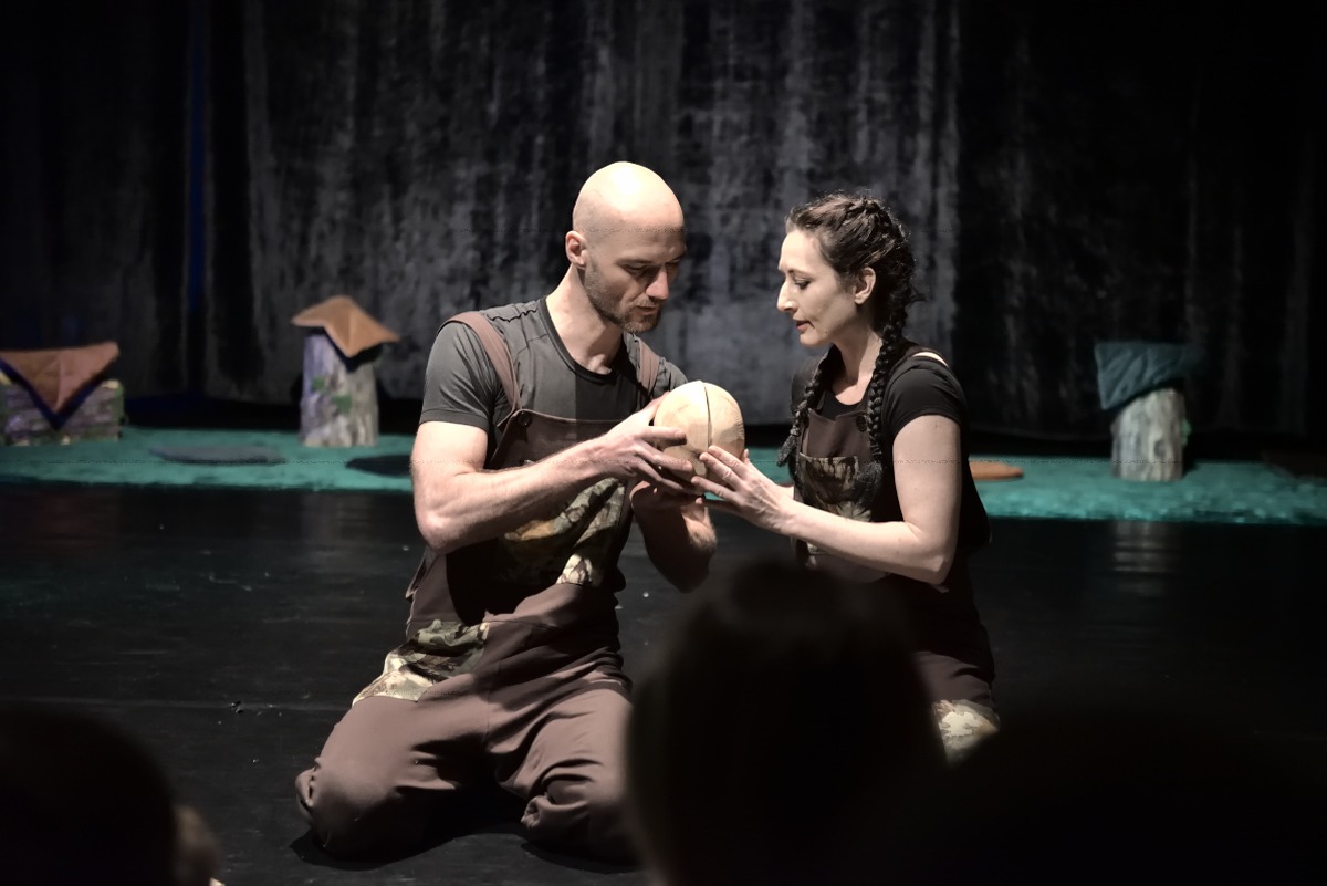 Mężczyzna i kobieta na scenie obserwują drewniane kule.