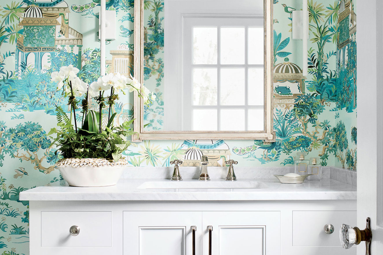 Elegant bathroom vanity with white marble top, white orchid plant, and teal chinoiserie wallpaper.
